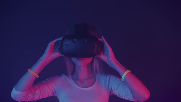 Portrait of Young Blondy Girl Wearing Virtual Reality Glasses, Looking Aside, Standing at Neon