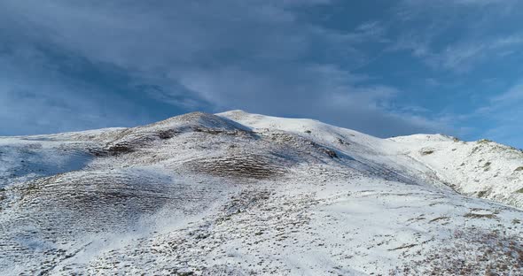 Forward Aerial Top View Over Winter Snowy Mountain Top in Sunny Day with Clouds and Blue Sky