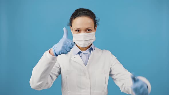 Female Doctor Wearing Protective Mask Showing Thumbs Up Gesture with Both Hands Blue Studio