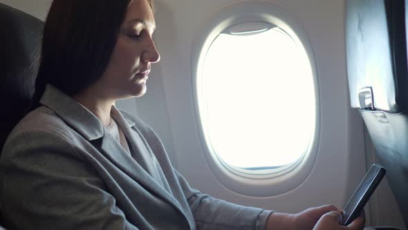 Brunette Woman Looking at the Phone While Sitting By the Airplane Window