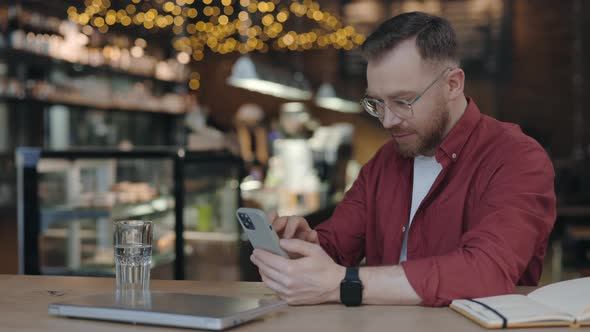 Guy is Using Smartphone for Messaging While Working at the Cafe