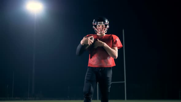 American Football Player Holds a Ball While Walking on a Field, Close Up.