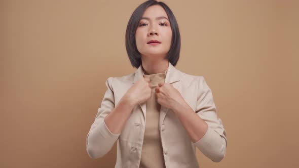 Happy asian business woman adjusting her suit and looking at camera like a mirror isolated