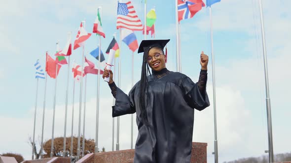 Young African American Woman Rejoices with a Diploma of Higher Education in Hand on the Street