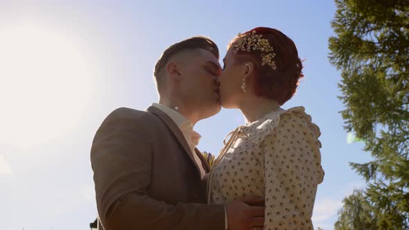 Beautiful Couple of Bride and Groom are Kissing Against Backdrop of Cloudless Blue Sky