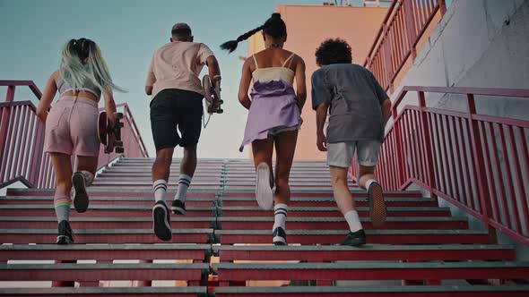 Group of Diverse Young People with Skateboard Running Up on Urban Staircase Together Enjoying Free