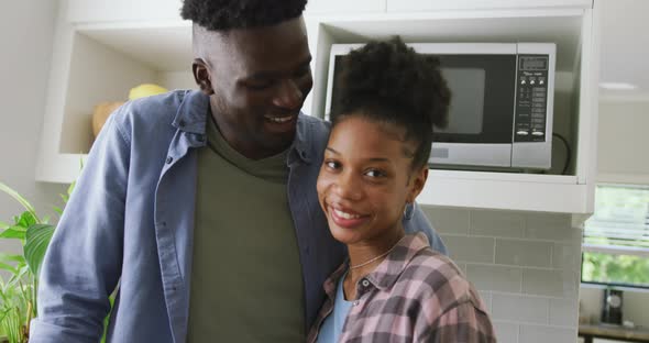 Video of happy african american couple embracing in kitchen and looking at camera