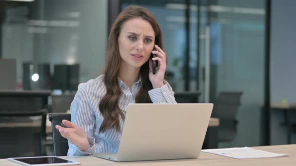 Angry Businesswoman Talking on Smartphone while using Laptop