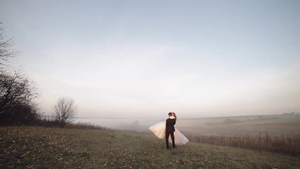 Newlyweds Dancing. Caucasian Groom with Bride on the Morning Field. Fog. Wedding