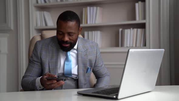 Rich Man Is Using Smartphone Sitting in His Luxury Office, Black Male Boss Dressed Expensive Suit
