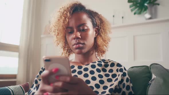 Young African American Woman Uses Mobile Phone for Online Shopping Sits on Sofa