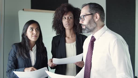 Three Business Partners Holding Documents and Discussing Project