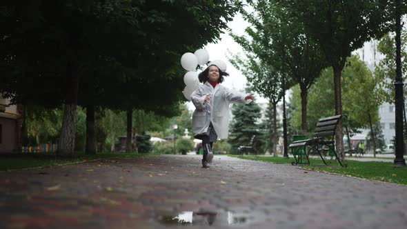 Wide Shot Excited Cheerful Little Person Jumping with Balloons Smiling Enjoying Leisure on Rainy Day