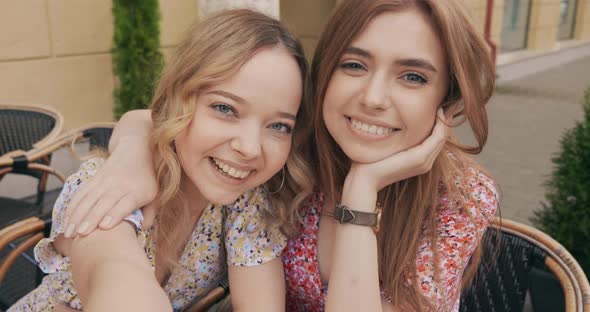 Two young beautiful smiling hipster girls in trendy summer sundress posing outdoors