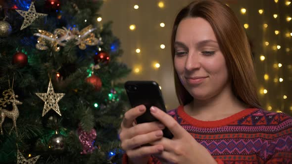 Woman In Knit Sweater Using Cell Phone Celebrating Christmas At Home