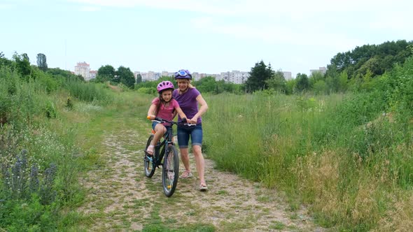 A mother teaches her daughter to ride a Bicycle in a Bicycle helmet. Safe Cycling.