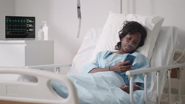 A Young Woman Writes a Message on Her Phone While Lying in a Hospital Ward alt