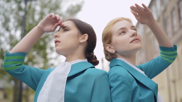 Two Confident Women Standing Back To Back and Holding Hands at Foreheads. Portrait of Slim Beautiful