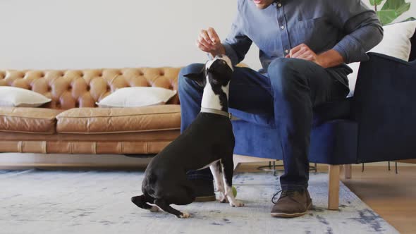 Happy caucasian man training and feeding his dog at home