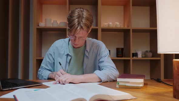 Man Studying at Home Looks at a Laptop Writes a Notebook and Reads a Textbook