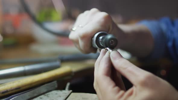 Close up of hands of caucasian female jeweller using tools, making jewelry