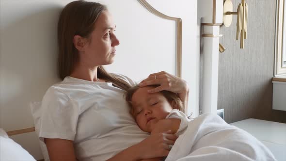 Mother Lying on Bed with Her Sleeping Child at Home