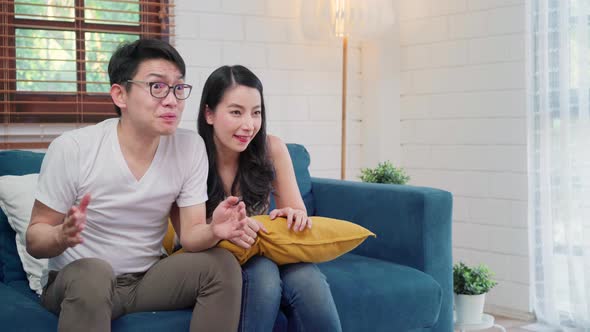Asian couple cheer football match in front of television living room at home.