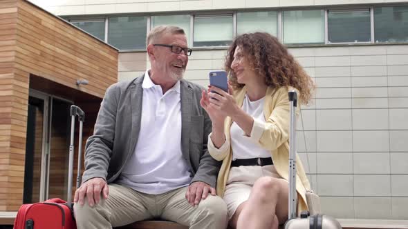 Beautiful Mature Couple with Suitcases is Sitting on a Bench While Waiting for Their Flight