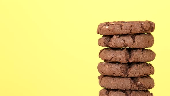 Stack of oatmeal cookies with cocoa, chocolate and hazelnuts rotating on yellow background