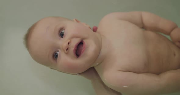 Portrait of Bare Infant Looking Up with His Blue Eyes and Smiling During Bathing