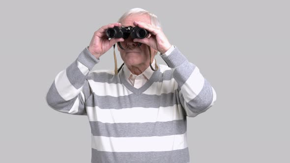 Elderly Man with Binoculars, Grey Background.