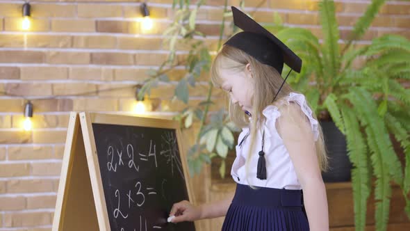 Little Girl Writes with Chalk on Chalkboard on Background of School Class