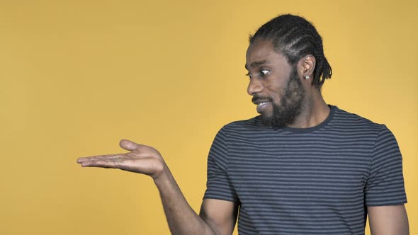 Casual African Man Showing Product at Side Yellow Background