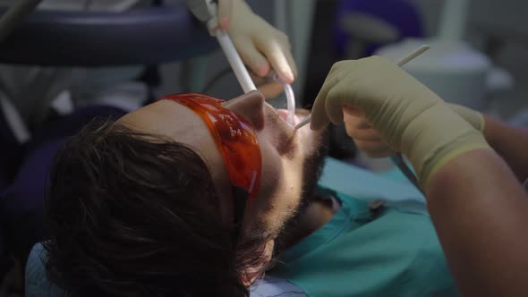 Woman Dentist in a White Uniform and White Gloves Treats a Man