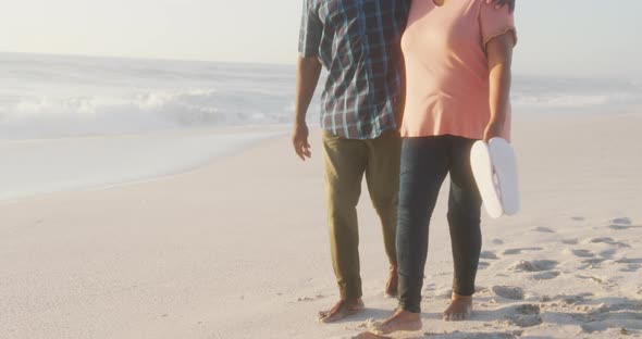 Smiling senior african american couple embracing and walking on sunny beach