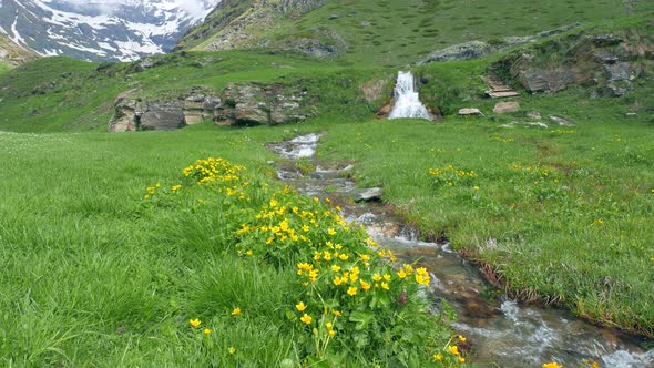 Slow motion: waterfall, stream flowing between green meadows
