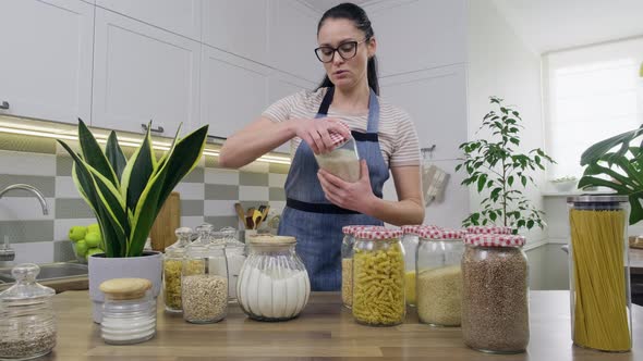 Storing Food in Kitchen Woman Housewife in an Apron with Jars and Containers