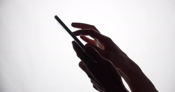 The silhouette of the fingers touches the smartphone screen. Mobile phone use.