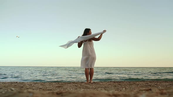 Young Woman in a White Dress Stands on the Seashore and Looks Into the Distance