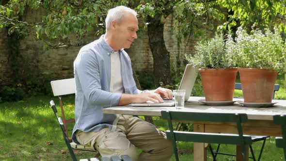 Mature male at table in garden working on laptop computer