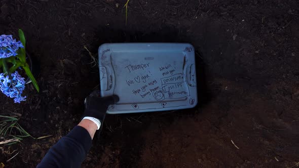 Placing the plastic case of the body of a dead family pet in a recently dug hole in a family garden