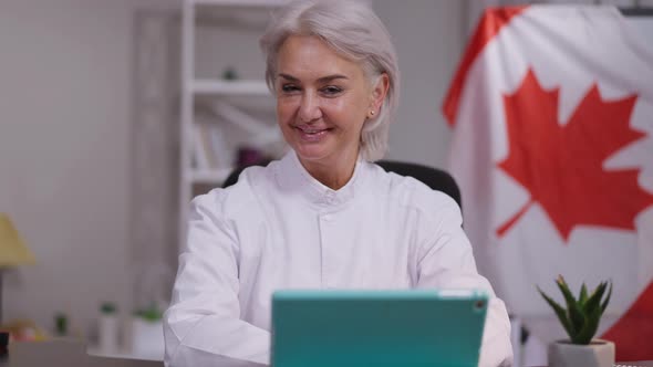 Joyful Mature Smiling Woman Talking Looking at Camera with Canadian Flag at Background