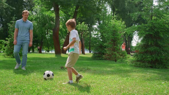 Sporty Man Passing Ball to Active Son on Green Park