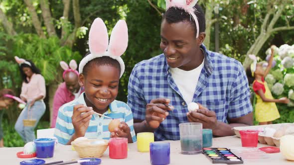 Animation of happy african american father and son painting easter eggs in garden