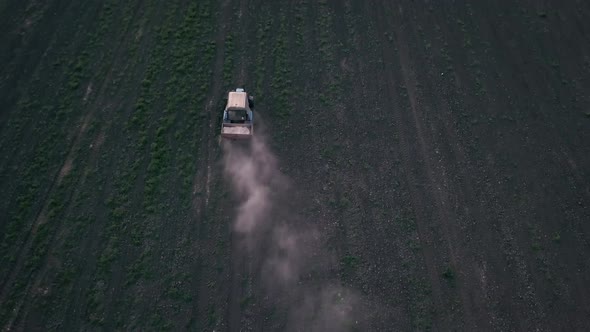 Aerial view of a farmer on a green tractor plowing the dusty arid soil. Agribusiness in the spring