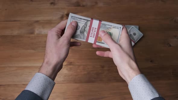 Stack of 10000 American Dollars Banknotes in Male Hands Over Wooden Background