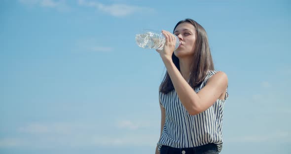 Young Woman Drinking Fresh Water on Sky with Clouds As Background on Sunny Day