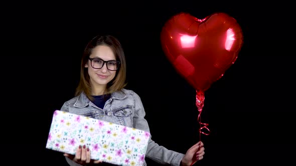 A Young Girl Is Standing with a Gift and Heart-shaped Balloons, A Woman Holds in Her Hands a Gift