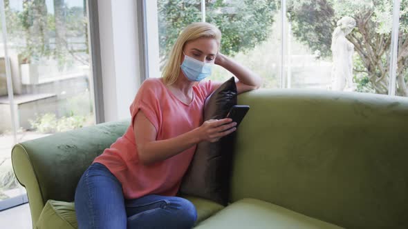 Woman wearing face mask using smartphone at home