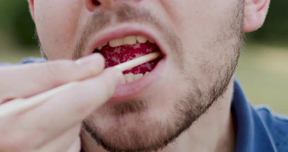 Closeup View of a Man Dressed in Blue Putting a Sushi in His Mouth Using Chopsticks